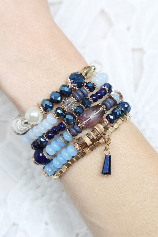 This is a photo of the Multi Sone Beads Stackable Bracelet in navy.  This bracelet features 6 strands of metal, acrylic, crystal bead, wood, and natural stone beads. in navy blue, white, gold and brown. 
